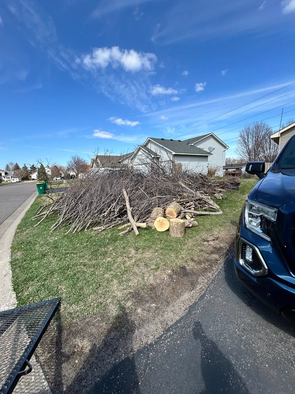 Tree branches and logs gathered beside a residential driveway for removal